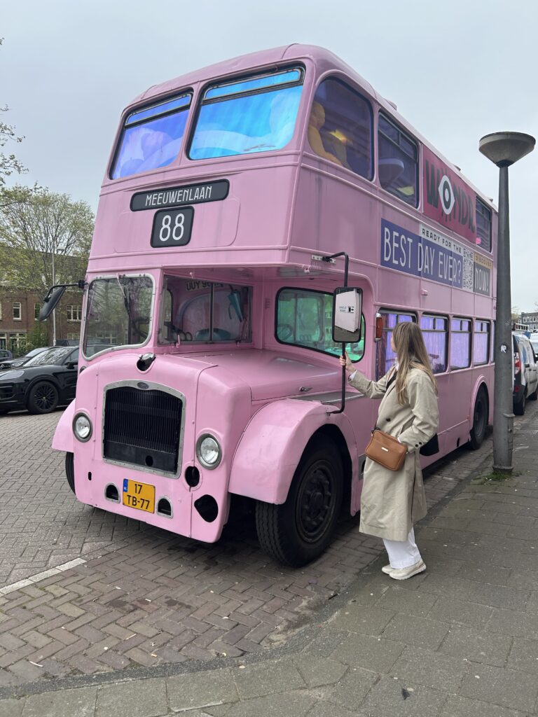 Person in front of a pink doble story bus